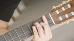 A hand plays a Barre F chord on an acoustic guitar